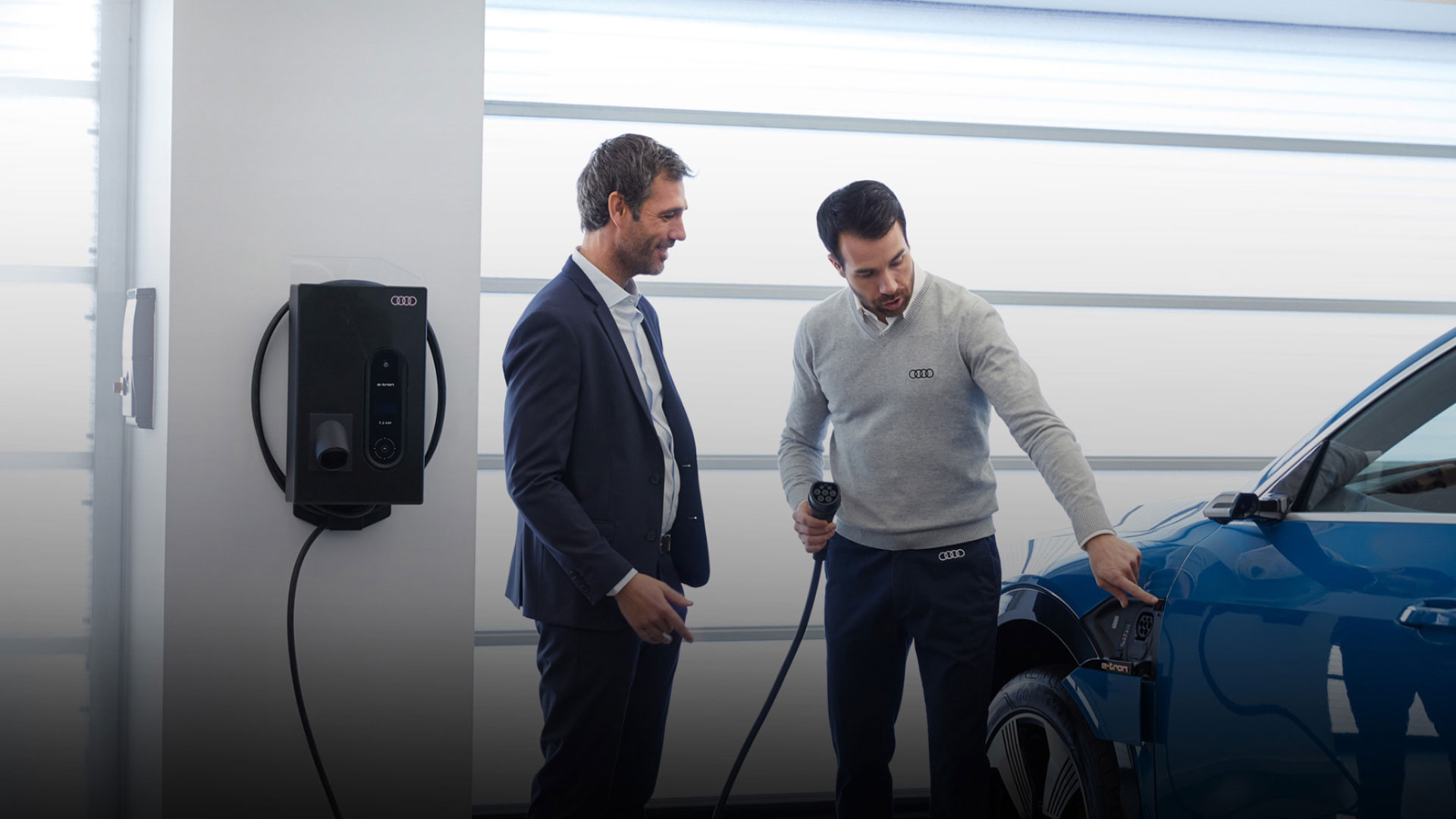 An Audi dealer showing a new Audi owner how to charge his EV. 